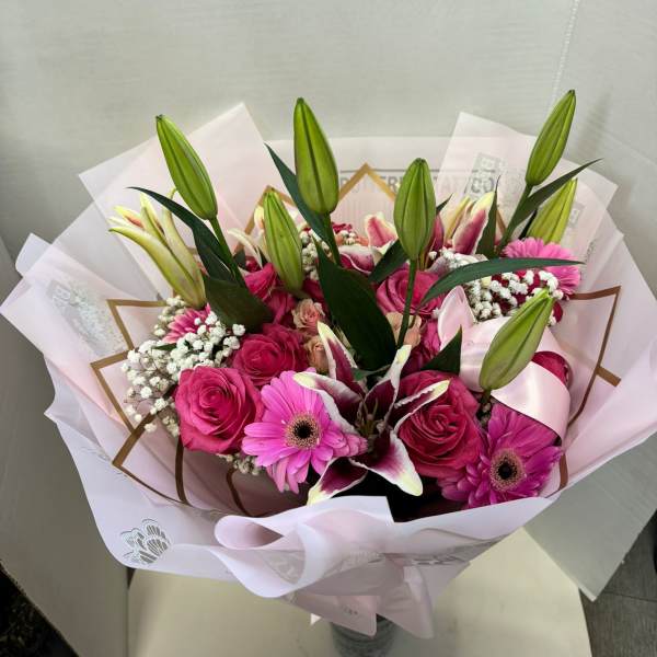 Pink bouquet with roses, lilies, and gerbera daisies wrapped in pale paper