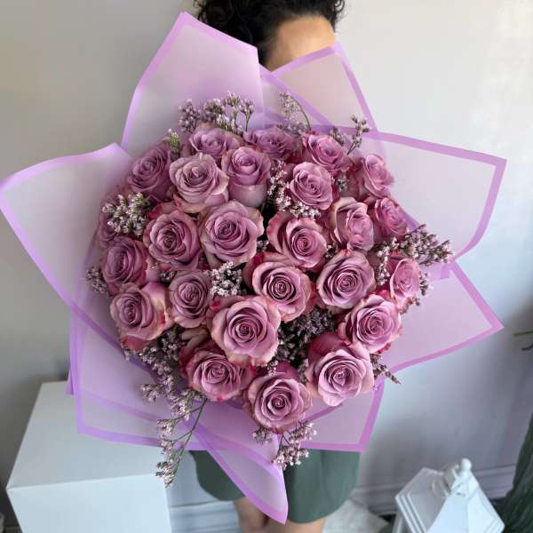 Large bouquet of lavender roses with small filler flowers wrapped in pink paper