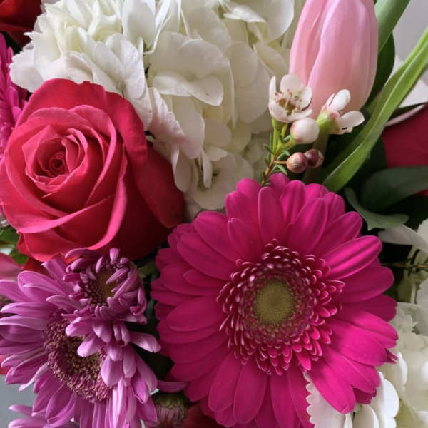 Close-up of a bright bouquet with hot pink gerbera daisy, pink and red roses, white hydrangeas, and a pale pink tulip