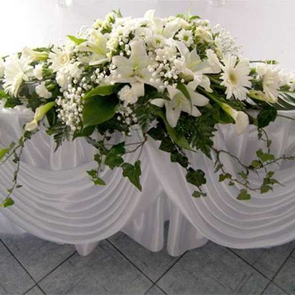 White floral arrangement with lilies and daisies on a draped table