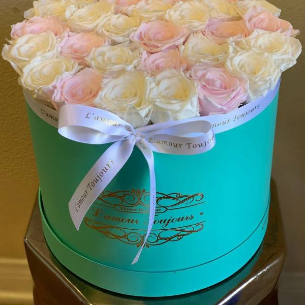 Pink and white roses arranged in a turquoise round box with a ribbon