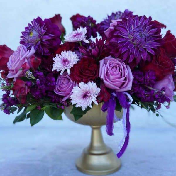 Purple and pink flower arrangement in a gold pedestal vase