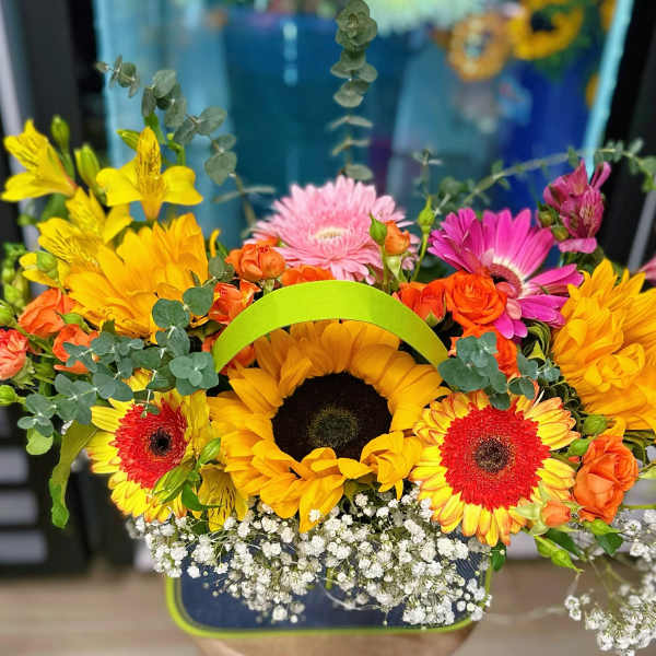 Bright mixed bouquet with sunflowers, gerbera daisies, and orange roses in a handled basket