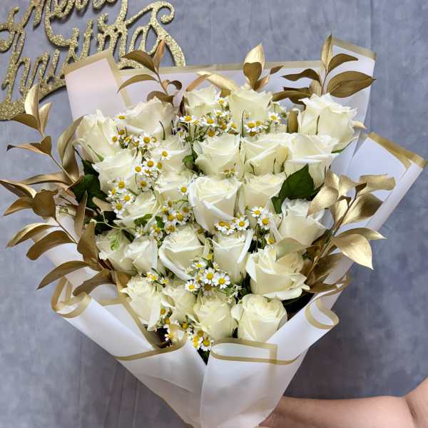 Bouquet of white roses and small daisy-like flowers wrapped in white paper with gold ribbon