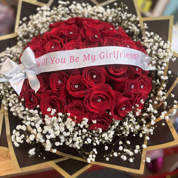 Red rose bouquet with baby's breath and a white ribbon reading "Will You Be My Girlfriend?"