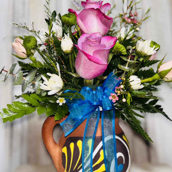 Pink roses and white daisies arranged in a painted ceramic jug with a blue ribbon