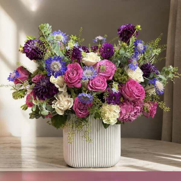 Mixed bouquet of pink, purple, and white flowers in a ribbed white vase