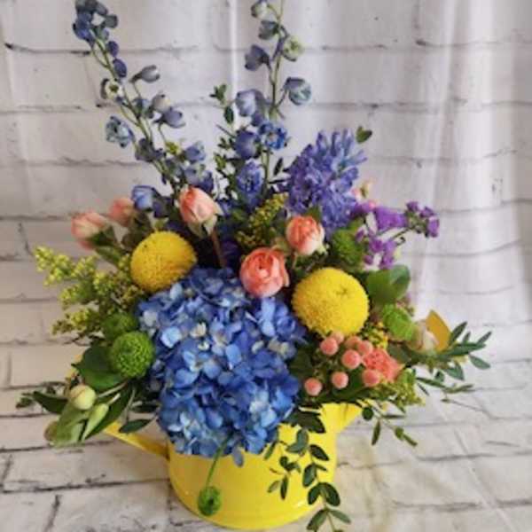 Colorful flower arrangement in a yellow container with blue hydrangea and mixed blooms