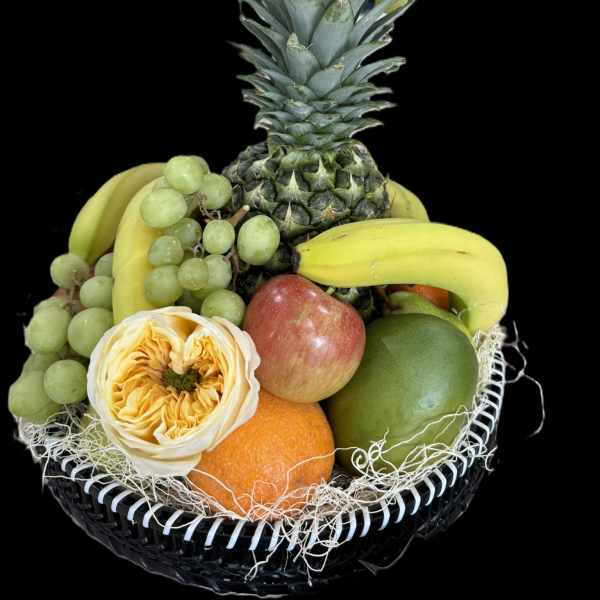 Fruit basket with pineapple, grapes, bananas, mango, orange, and a rose