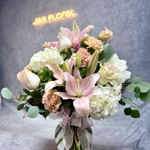 Pink lilies and white hydrangeas in a glass vase with a ribbon
