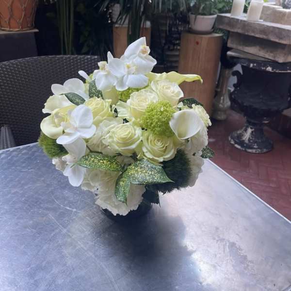 White floral arrangement with roses, orchids, and calla lilies in a dark vase