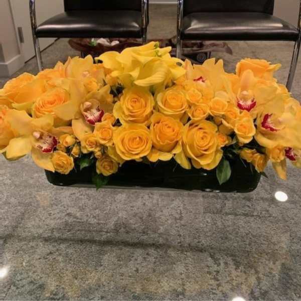 Yellow roses and orchids arranged in a low rectangular container