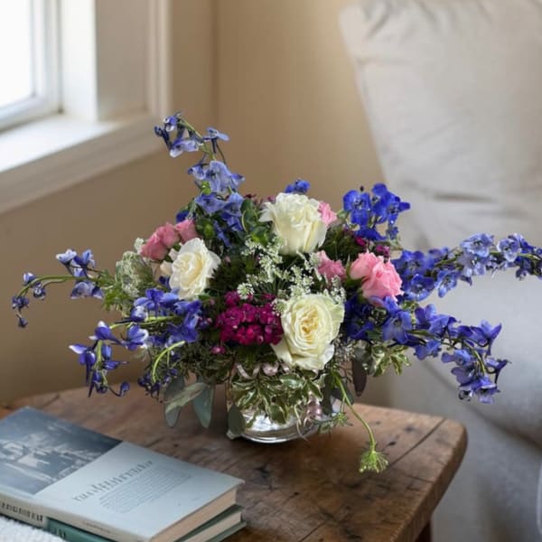 Bouquet of pink and white roses with blue flowers in a glass vase
