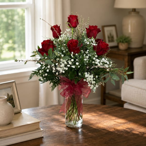 Red roses in a clear glass vase with white filler flowers and a burgundy ribbon