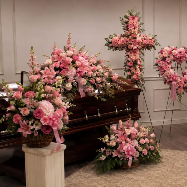 Pink funeral floral arrangements around a casket in a chapel