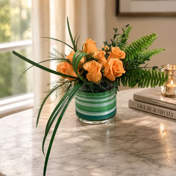 Orange roses in a striped glass vase with long green foliage