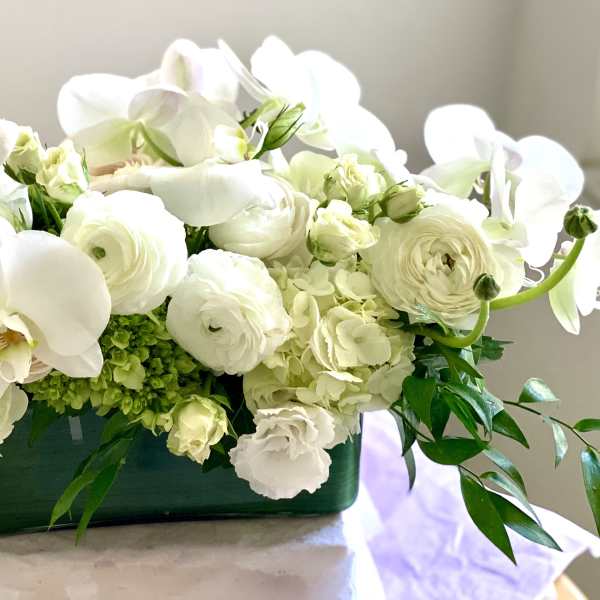 White orchids and pale blooms arranged in a green container