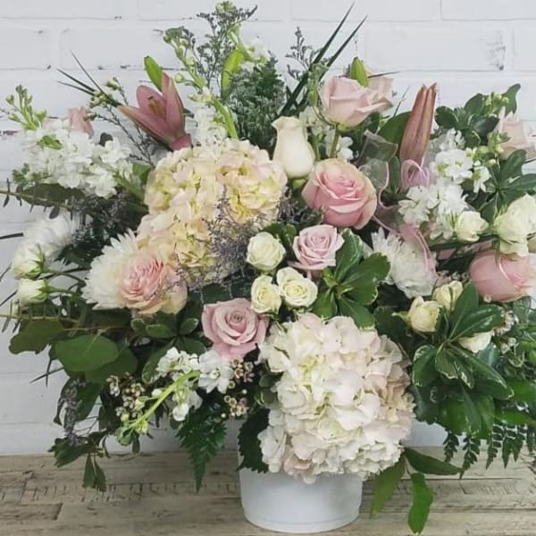 Large pastel bouquet with roses, hydrangeas, and lilies in a white container