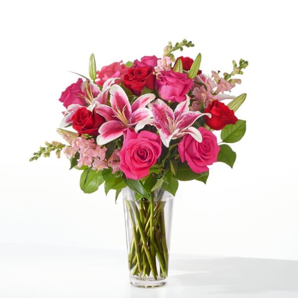 Pink and red roses with lilies in a clear glass vase