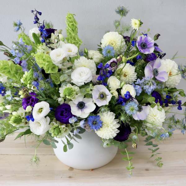 Mixed white, blue, and purple flowers in a white bowl vase