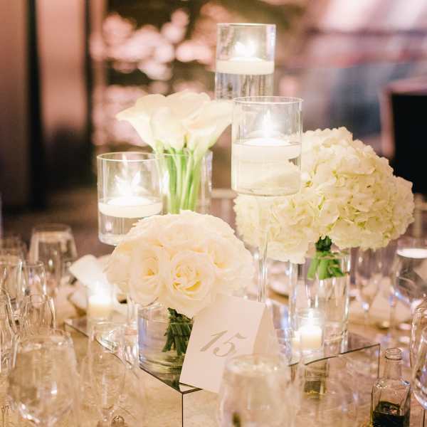 White floral centerpieces with candles in glass cylinders on a table