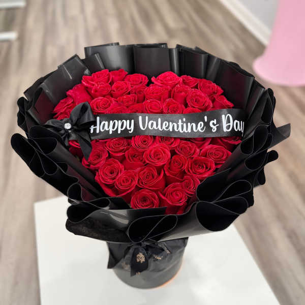 Bouquet of red roses wrapped in black paper with a Valentine’s Day ribbon