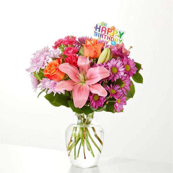 Pink and orange mixed bouquet in a glass vase with a Happy Birthday pick
