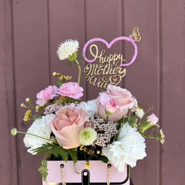 Pink and white floral arrangement in a pink handbag box with a "Happy Mother's Day" topper