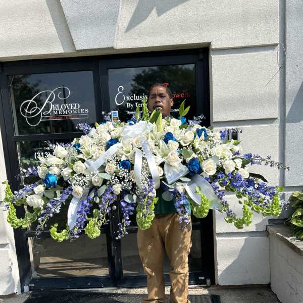 Large funeral spray of white and blue flowers with trailing purple blooms