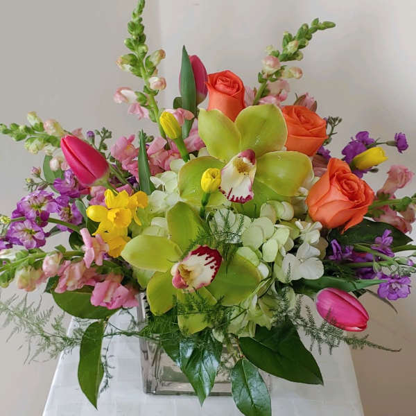 Mixed bouquet with orange roses, green orchids, and pink tulips in a glass vase