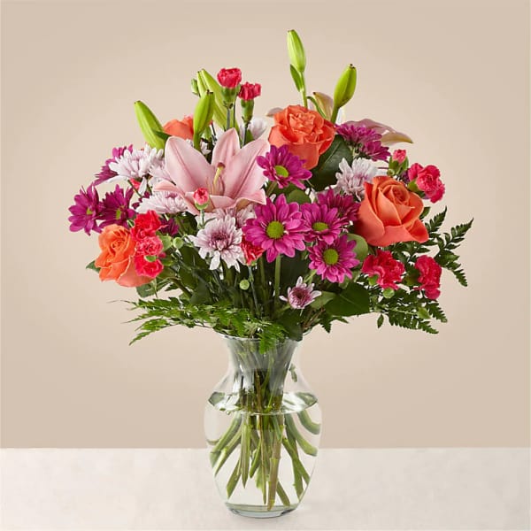 Bouquet of pink lilies, orange roses, and magenta daisies in a glass vase