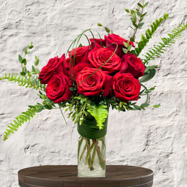 Red roses arranged in a clear glass vase with fern accents