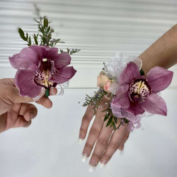 Two purple orchid wrist corsages held in hands.