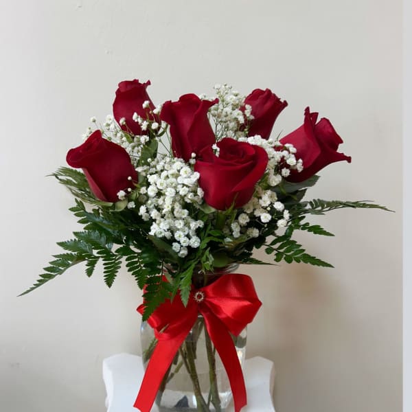 Red roses in a glass vase with baby's breath and a red ribbon