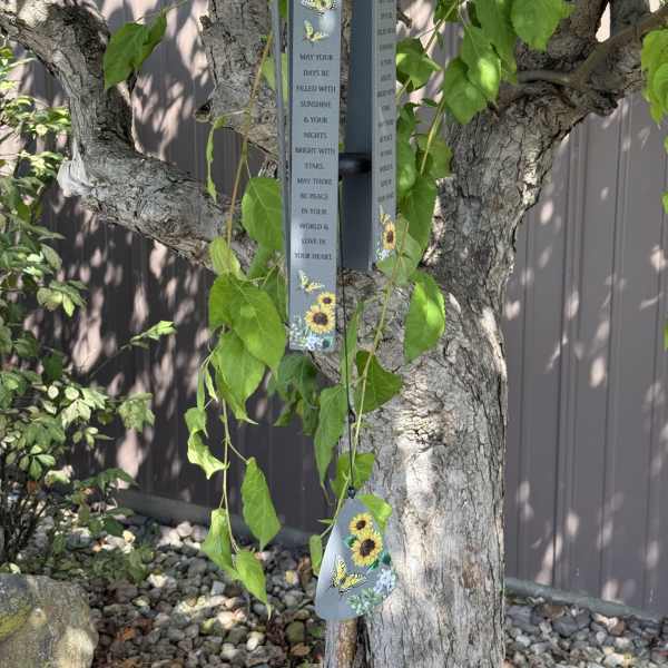 Hanging metal wind chime with butterfly and sunflower designs on a tree
