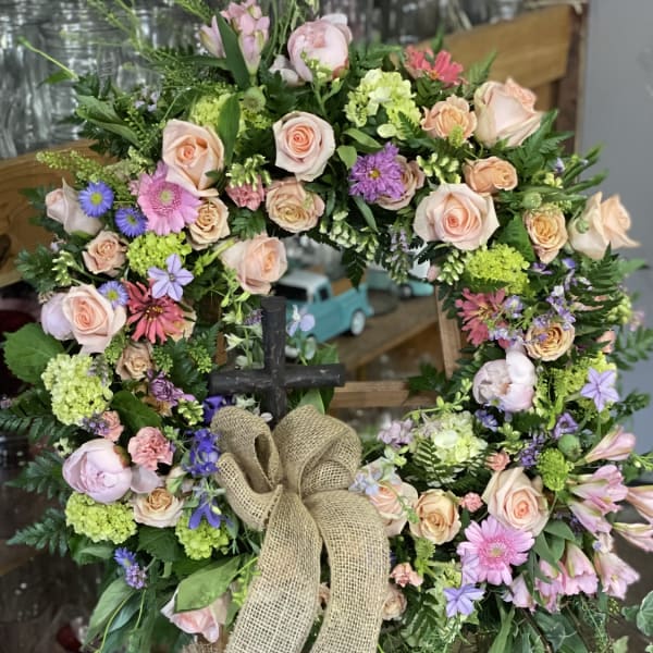 Floral wreath with pastel roses, daisies, and a burlap bow on an easel