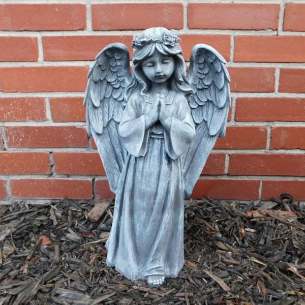 Stone angel statue with folded hands in front of a brick wall