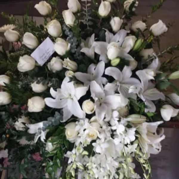Large white funeral spray on an easel with lilies and roses