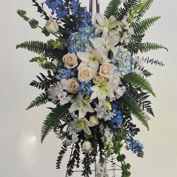 Standing floral spray with white lilies, blue flowers, and a cross