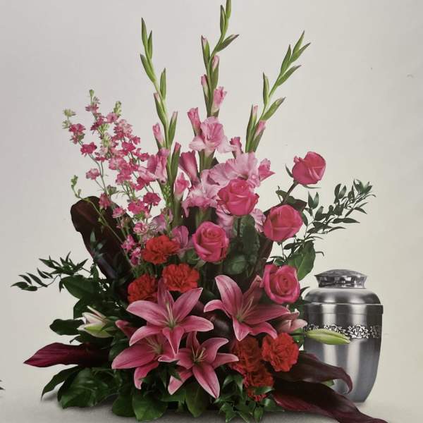 Pink lilies and roses arranged with red carnations beside a silver urn.