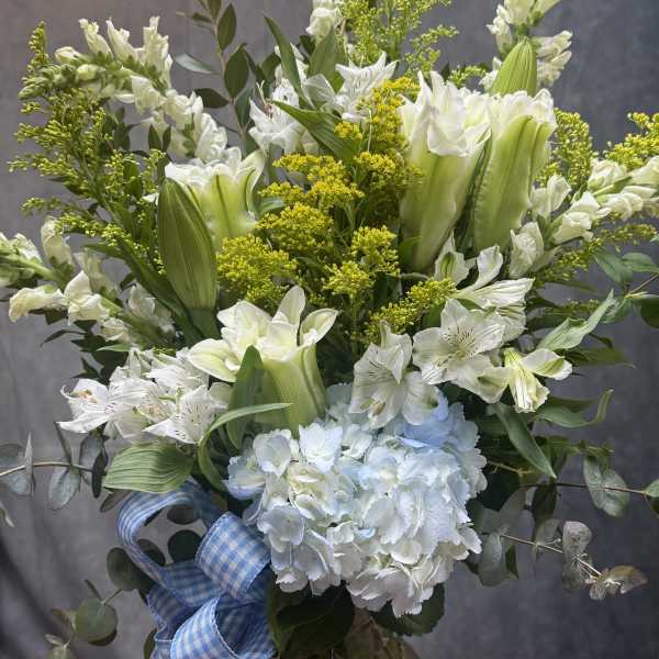 White and pale green floral arrangement in a glass vase with a blue ribbon