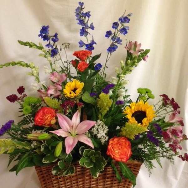 Mixed flower arrangement in a wicker basket with sunflowers, lilies, and roses