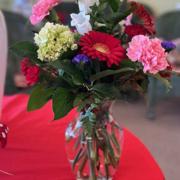 Mixed bouquet of gerbera daisies, carnations, hydrangea, and white bell-shaped flowers in a glass vase
