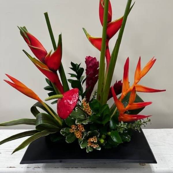 Tropical flower arrangement with red and orange heliconia in a black tray