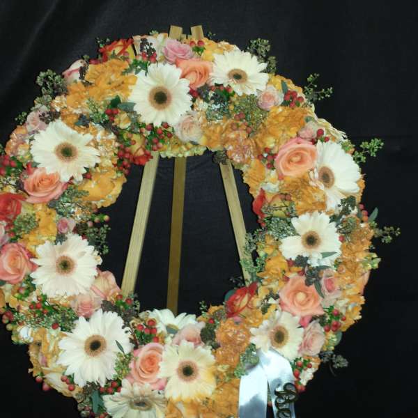Floral wreath with white daisies, peach roses, and orange blooms on a stand
