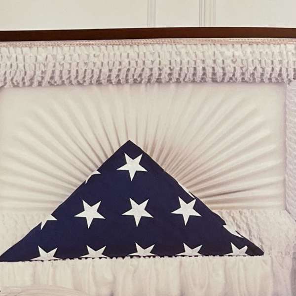 Casket spray with red roses, white lilies, and blue flowers beside a folded flag