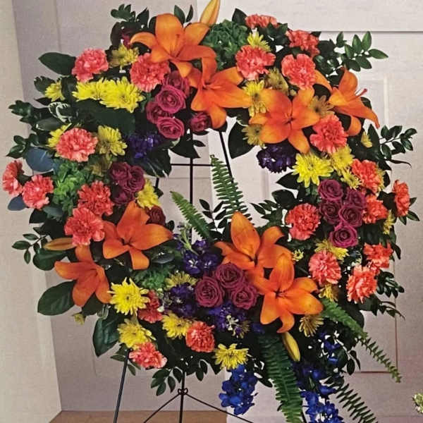 Large floral wreath with orange lilies, pink roses, and yellow and coral blooms
