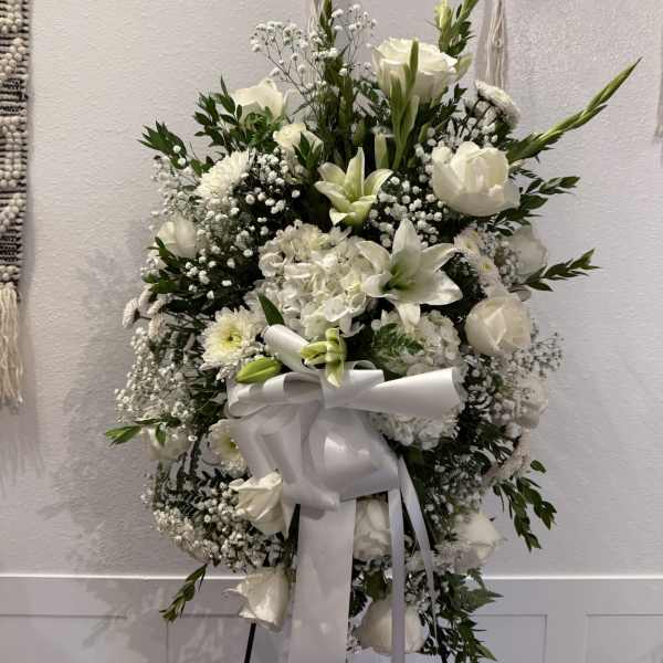 White funeral spray with lilies, roses, and a large ribbon on an easel