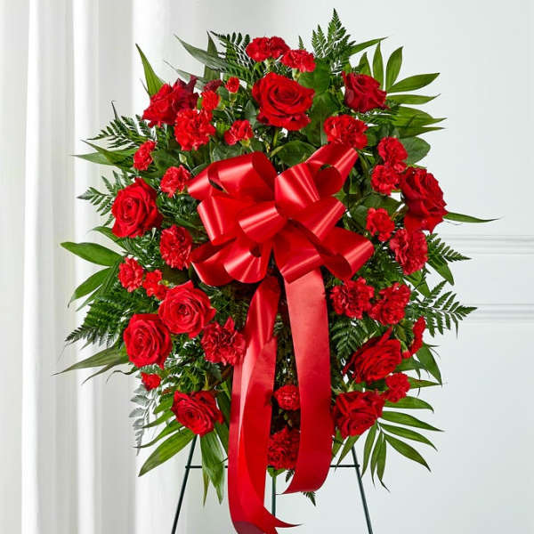 Red roses and carnations in a standing spray with a large red bow