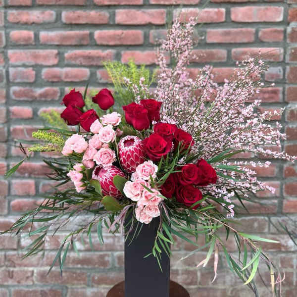 Red and pink floral arrangement in a tall black vase